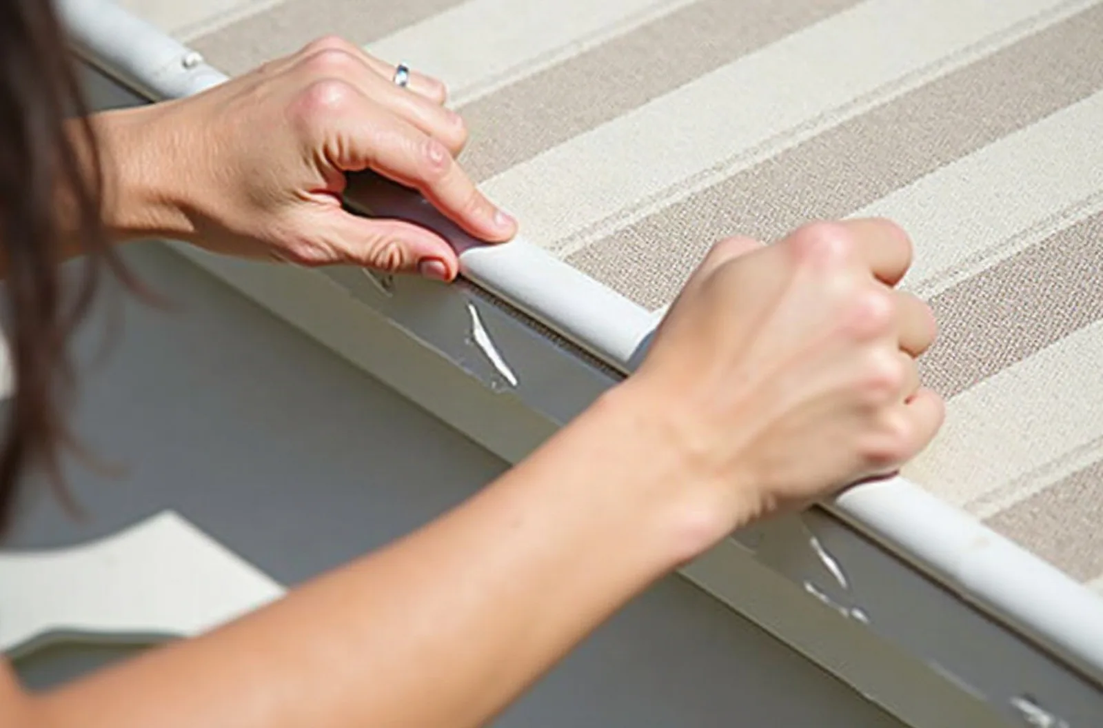 Hands applying clear repair tape to a small tear in striped awning fabric, a simple fix for RV awning repair.