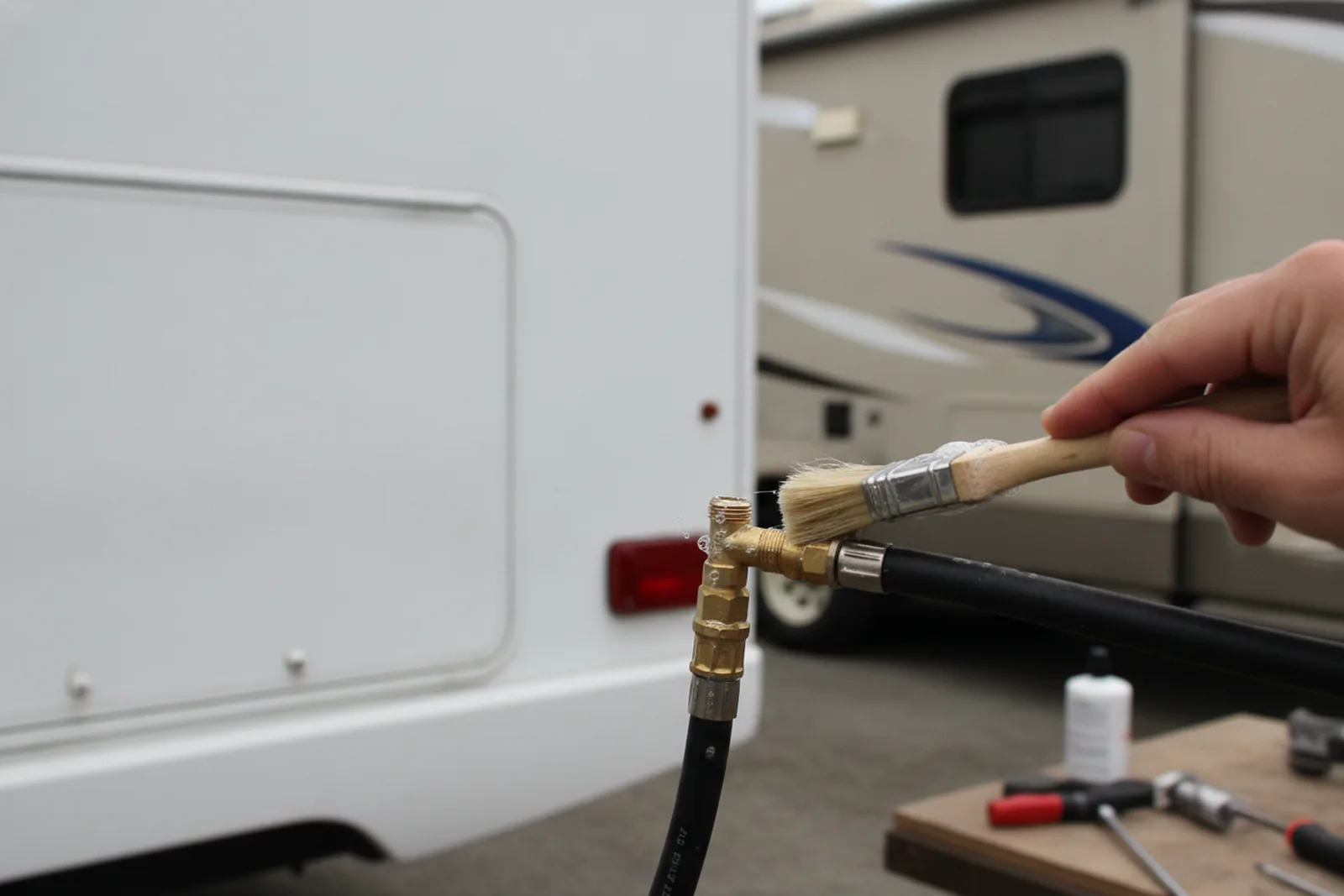 A hand applying soapy water to a propane hose fitting, with small bubbles indicating a leak during RV propane tank repair.